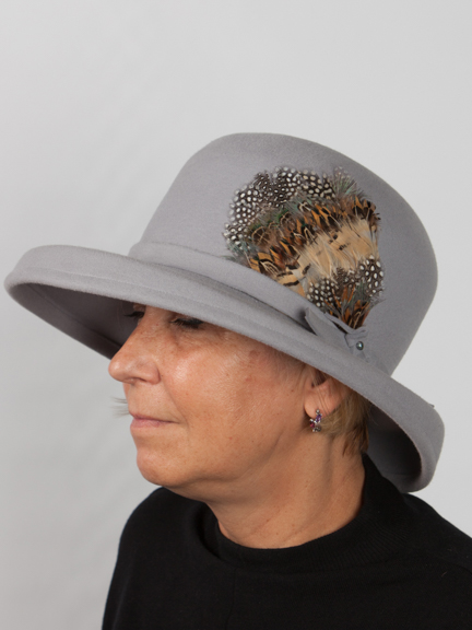 Side iew of large smokey grey felt hat with brim and feather deail to the side.