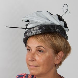 Side view of dark navy and white fabric occasion hat withquill and matching fabric design on top