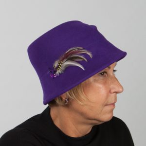 Side view headshot of purple woo felt hat with crease on the top and feather detail on the side