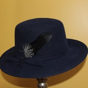Side view of large navy fur felt hat with black an speckled feather on the sideand felt band around crown