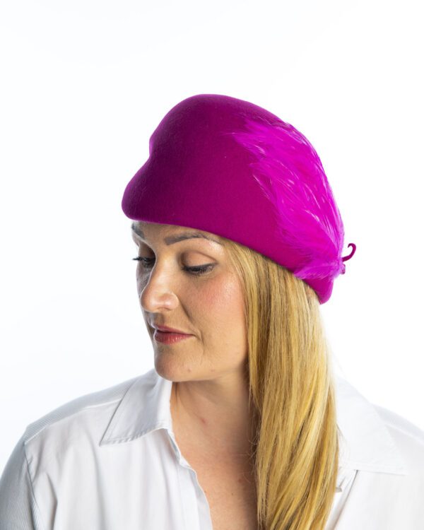 Side view of cerise wool felt hat with feather detail.